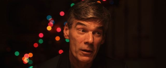 Still from Forgive Us, a tense close-up lit by Christmas lights